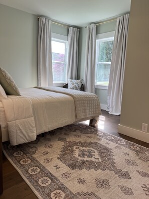 A bedroom with a bed, a patterned rug, and a window with curtains.