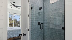 Ein modernes Badezimmer mit Duschkabine aus Glas, einem Bett mit gemustertem Überwurf und einem Deckenventilator.