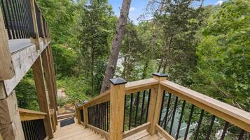 A wooden deck with a railing overlooking a forested area.