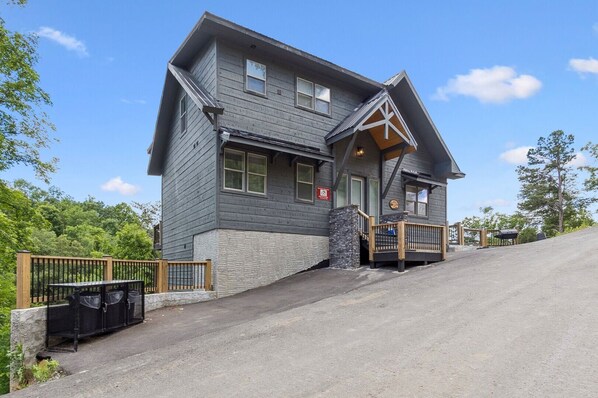 A two-story lodge with a stone foundation, a wooden deck, and a steep driveway.