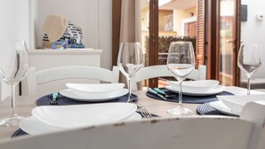 Ein Esstisch ist gedeckt mit weißen Tellern, blauen Untersetzern und Weingläsern, im Hintergrund ist ein Balkon und ein Außenbereich zu sehen.