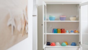 Ein weißes Schrank mit mehreren Regalen, gefüllt mit bunten Schüsseln und Tassen.