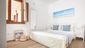 Ein Schlafzimmer mit einem Bett, Nachttischen, einem Spiegel, einem Gemälde und einem Korbwägelchen.