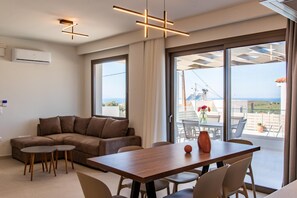 A modern living room with a sofa, round tables, and a wooden dining table. - Athel Panoramic View Villas Niki (Rethymno)