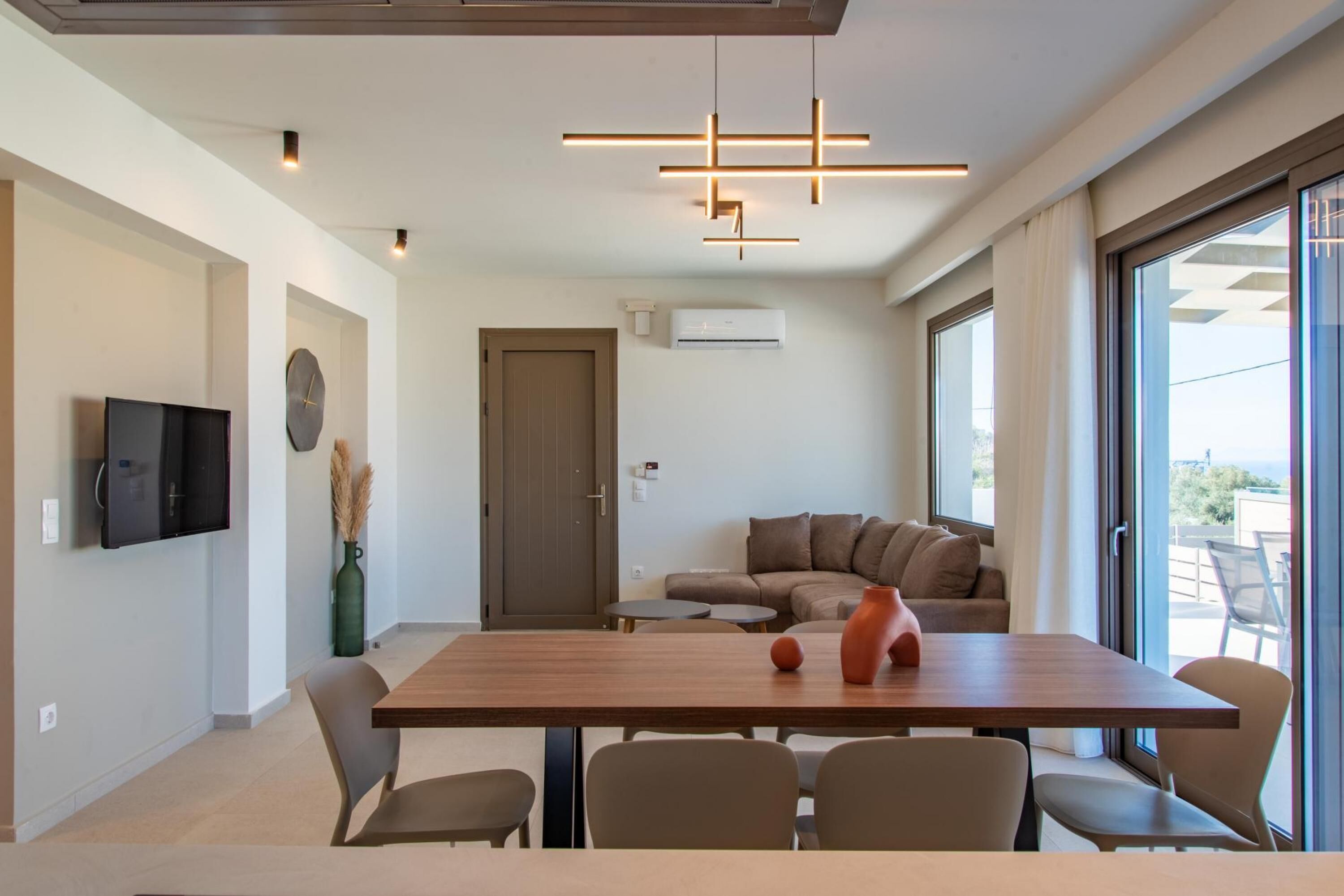 Una sala de estar moderna con una mesa de comedor de madera, sofás color beige y un televisor de pantalla plana montado en la pared.