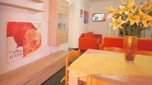 A dining area with a wooden table, chairs, a vase with flowers, and a television on the wall.