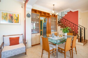 A dining area with a glass table, wooden chairs, a sofa with a cushion, a potted plant, and a staircase with a railing. - Villa Poros in Ionian Islands (Corfu)
