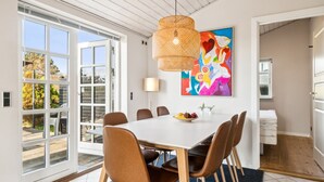 En matplats med ett stort bord, sex stolar, en hängande lampa och en färgstark, abstrakt målning på väggen.