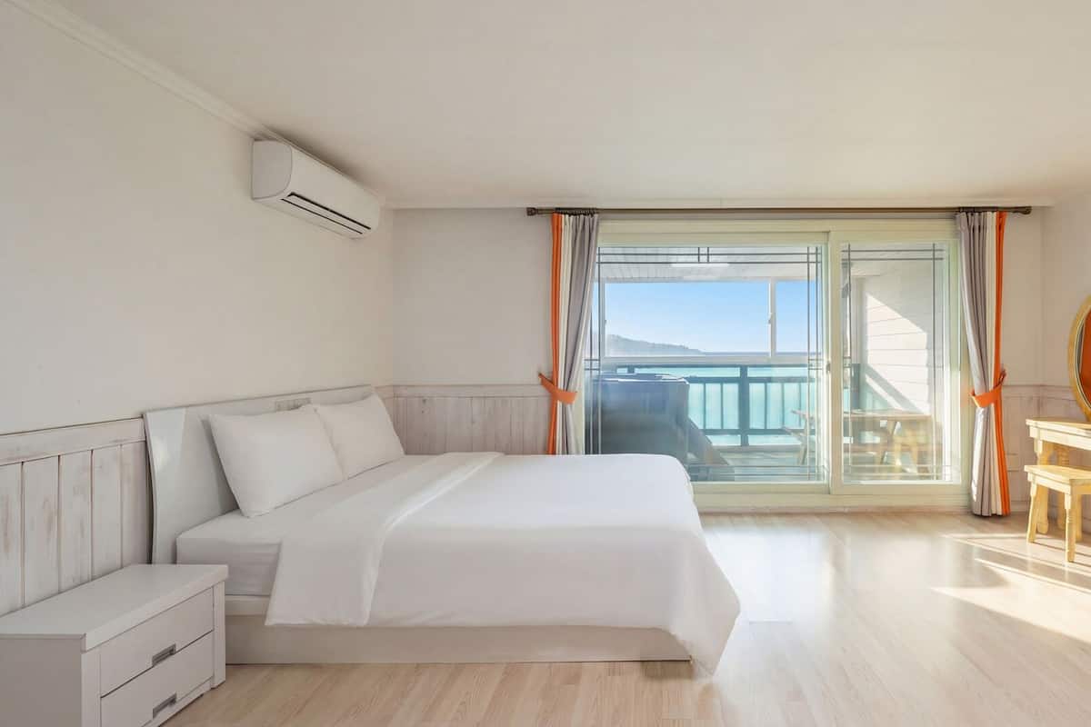 A hotel room with a bed, a TV, a wooden dresser, and a balcony with a view.