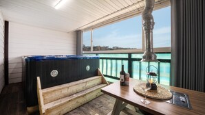 A wooden deck with a hot tub, a table with a glass of wine, and a view of the water. - Ganghwa Nakjogaboineun spa Pension (Incheon)