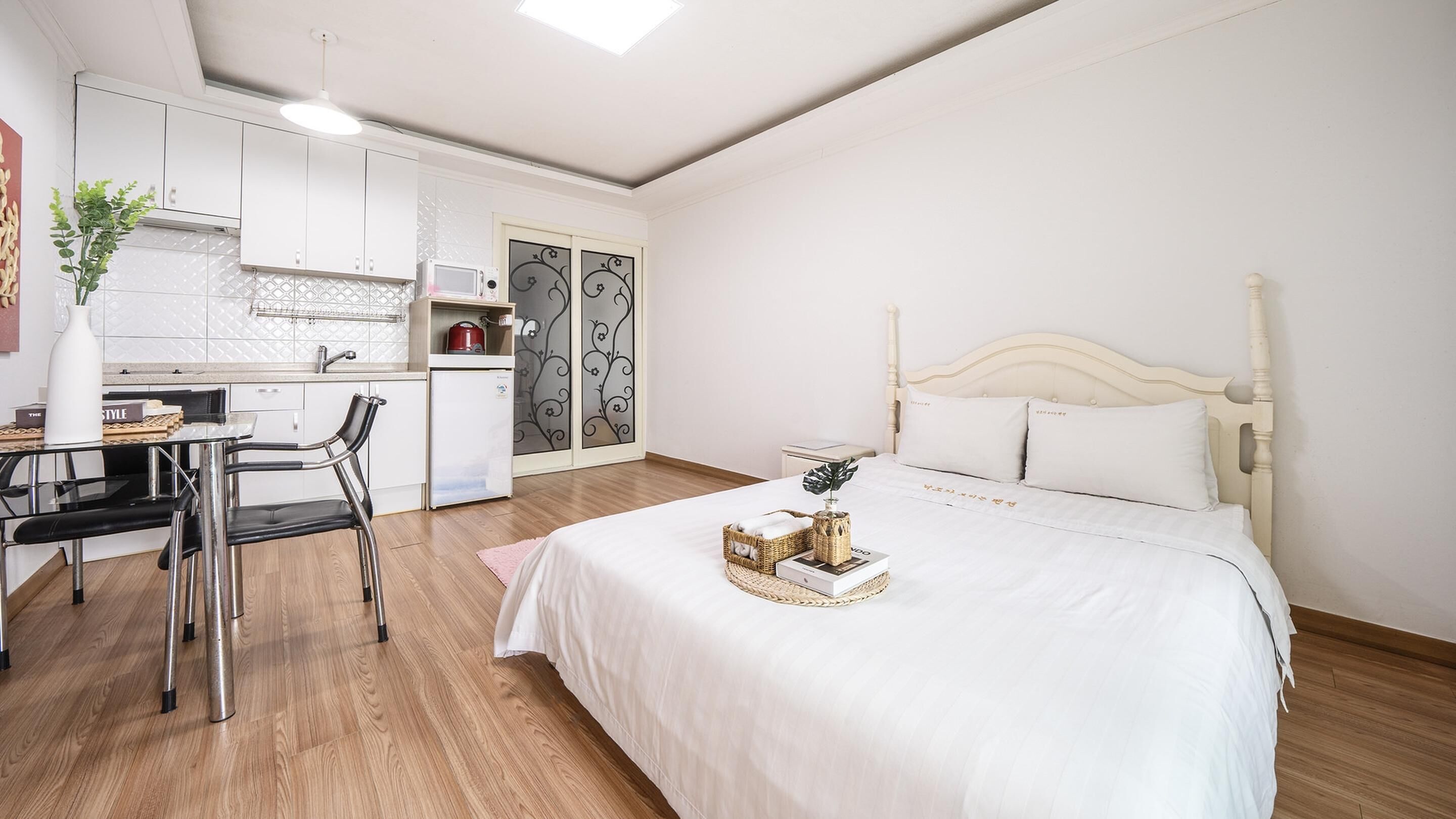 Une chambre d’hôtel de taille réduite, comprenant un lit, un petit bureau avec une chaise, une kitchenette et une salle de bain.