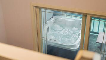 Un jacuzzi con chorros de agua, una terraza de madera en el exterior y un cerramiento de cristal.