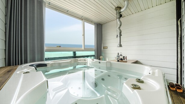 A large, clear hot tub with a view of the ocean through a window. - Ganghwa Nakjogaboineun spa Pension (Incheon)