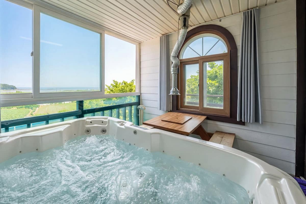 A hot tub with a wooden deck and a view of the countryside.