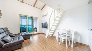 A modern living room with a leather sofa, a dining table with chairs, a TV mounted on the wall, and a staircase leading to an upper level. - Ganghwa Nakjogaboineun spa Pension (Incheon)