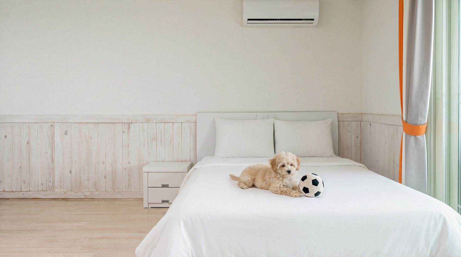 A bedroom with a bed, a small white nightstand, a wall-mounted air conditioner, and a window with curtains.