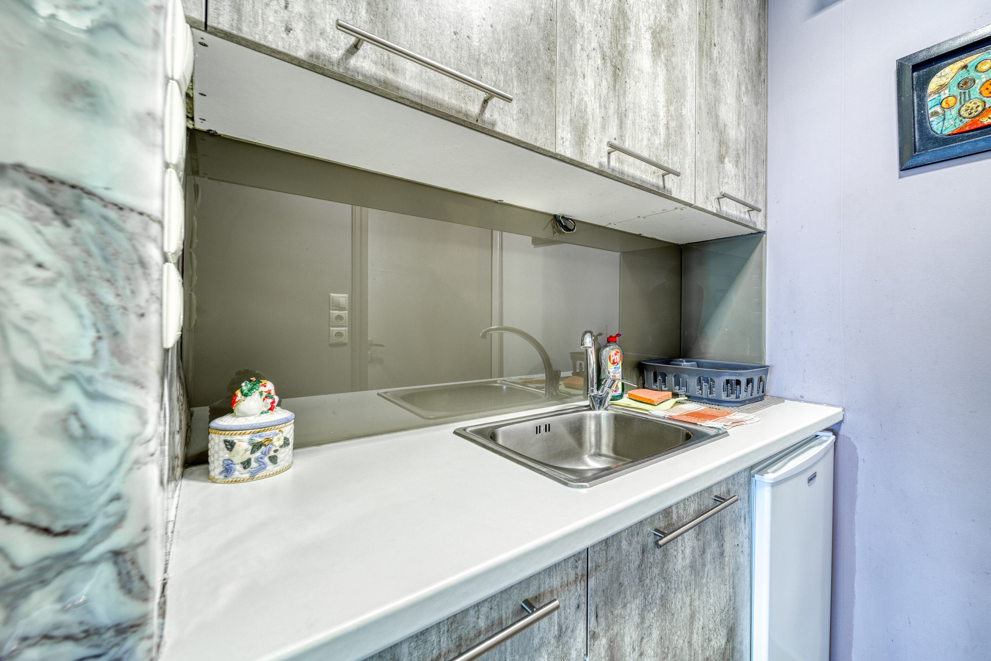 A kitchen with a white countertop, stainless steel sink, and a refrigerator.