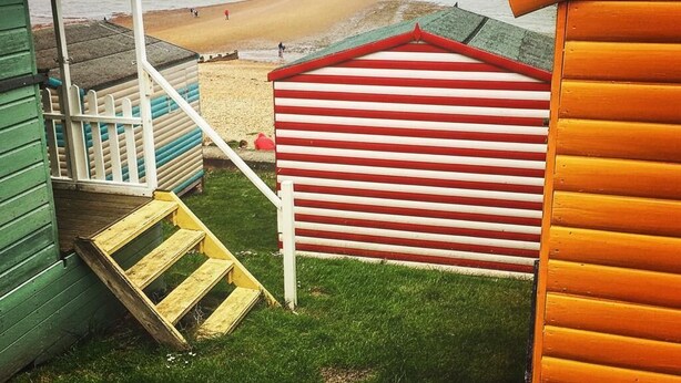 A beachside view with a wooden staircase leading to a beach, a red and white striped building, and a green structure.