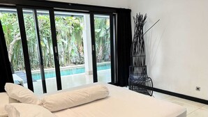 A bedroom with a bed, a view of a swimming pool, and a black metal chair. - Villa Adam Seminyak (Seminyak)