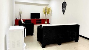 A modern living room with a flat-screen TV, a black sofa, a red entertainment unit, and a ceiling fan. - Villa Adam Seminyak (Seminyak)