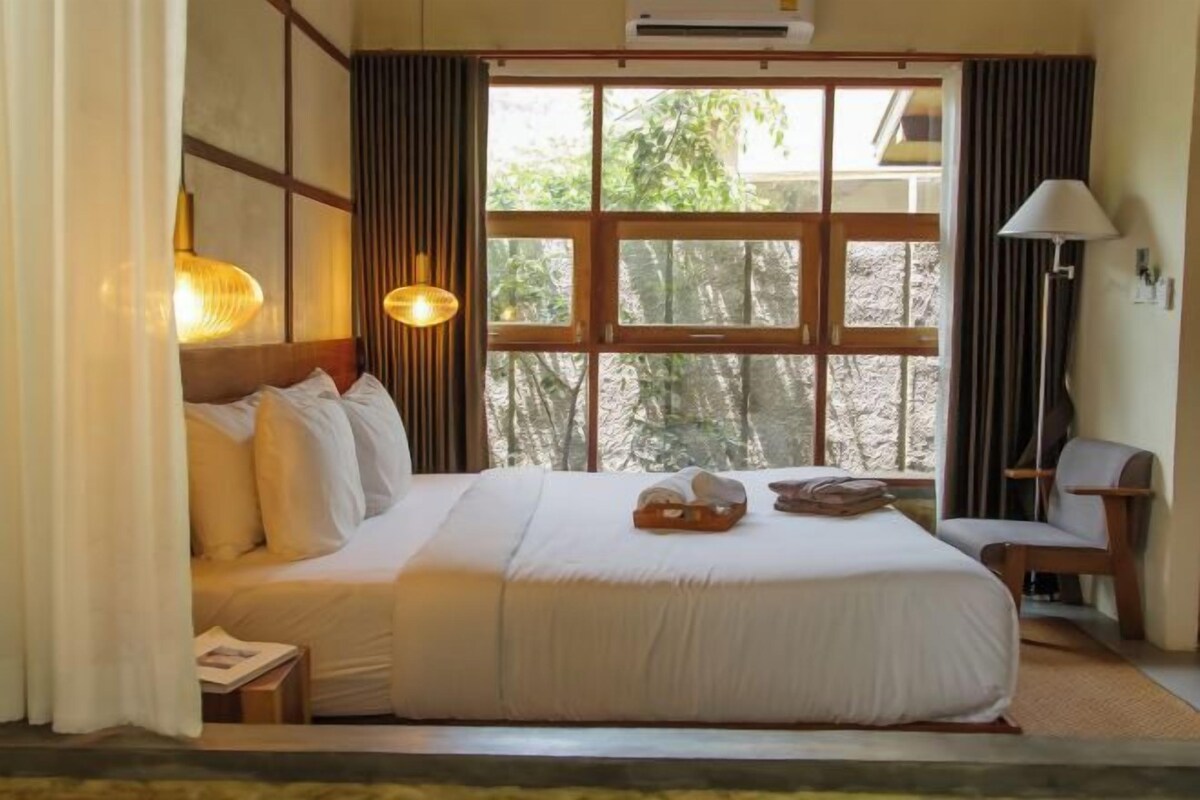 A hotel room with a large bed, a desk, a chair, and a window with curtains.