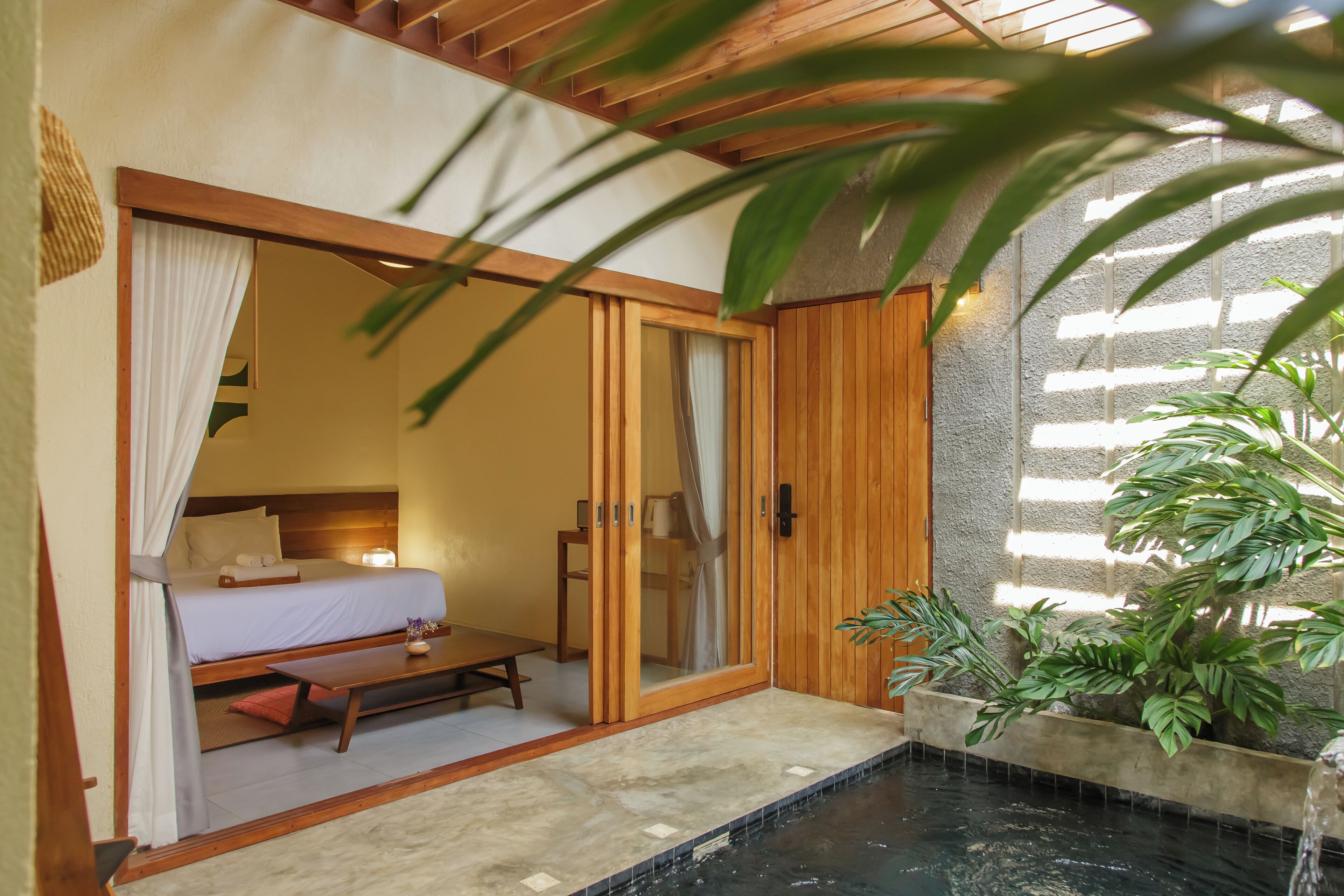 A room with a bed, a table, a bench, a small indoor water feature, and potted plants.
