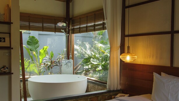 A bedroom with a large bed, a bathtub, and a window with curtains.