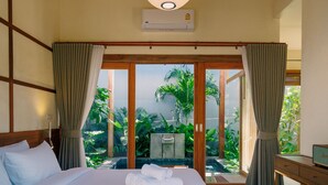 A hotel room with a bed, curtains, an air conditioning unit, a desk, and a view of a garden.