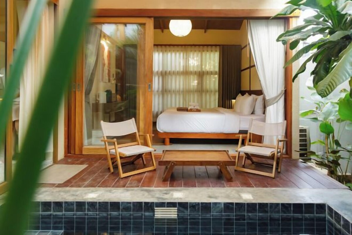 Un dormitorio con cama, dos sillones, una mesita y vista a una piscina.