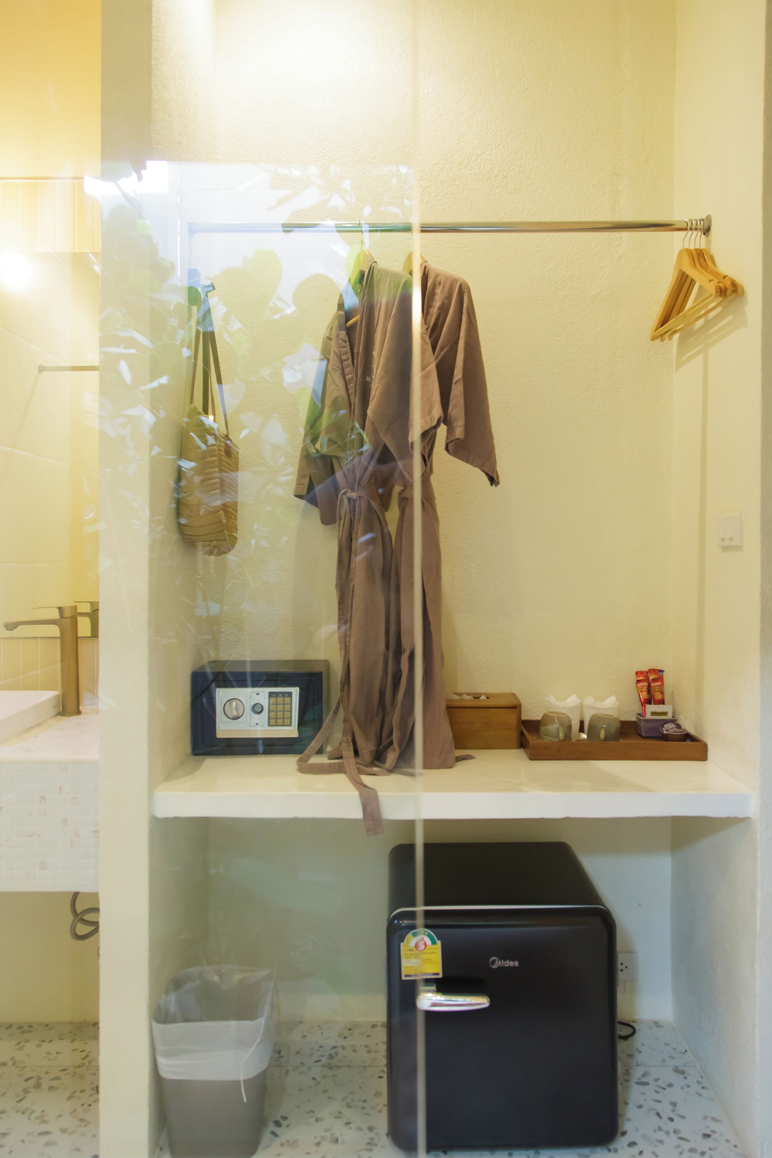 A bathroom with a towel rack, a radio, a trash bin, and a suitcase.