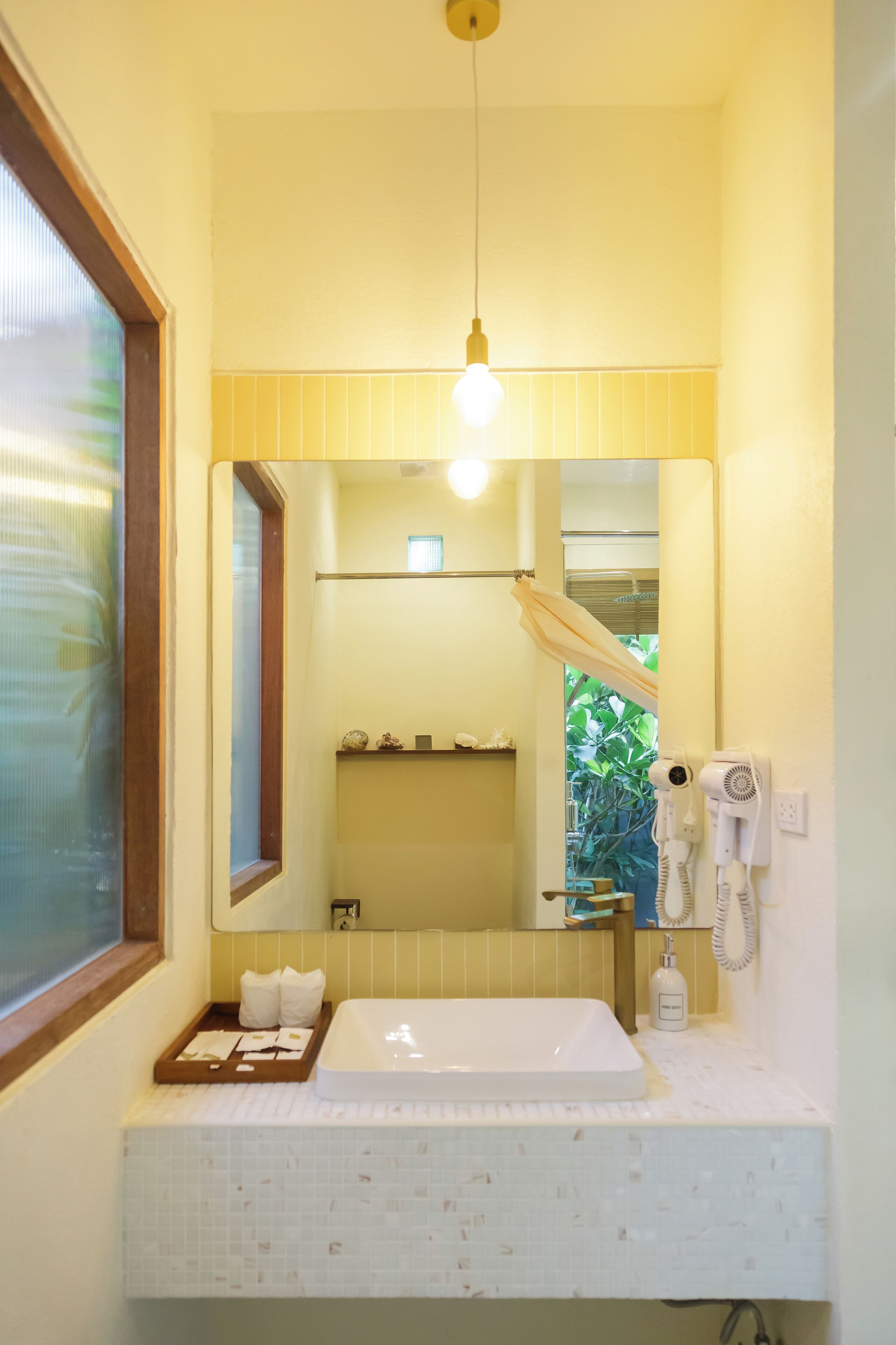 Un baño con lavamanos blanco, espejo, toallero y secador de pelo.
