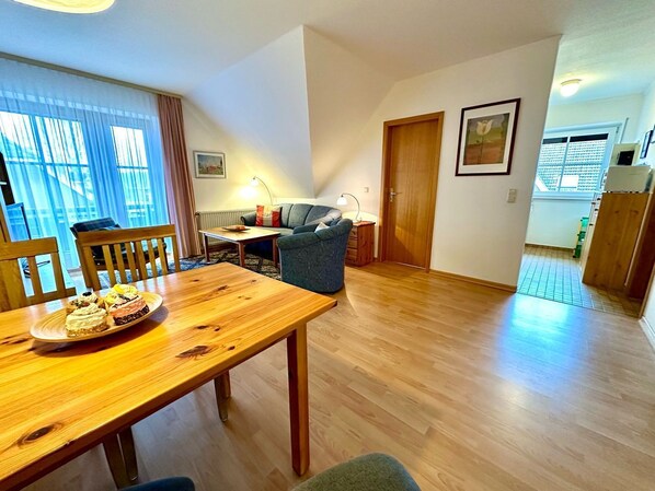 A room with a wooden dining table, a sofa, a lamp, and a door leading to a balcony.