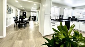 Una cocina amplia con armarios blancos, un comedor con mesa y sillas, y vistas al exterior gracias a amplios ventanales.
