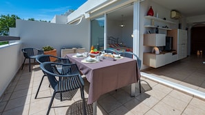 Un balcon avec une table dressée pour le repas, des chaises et un pot de fleurs.