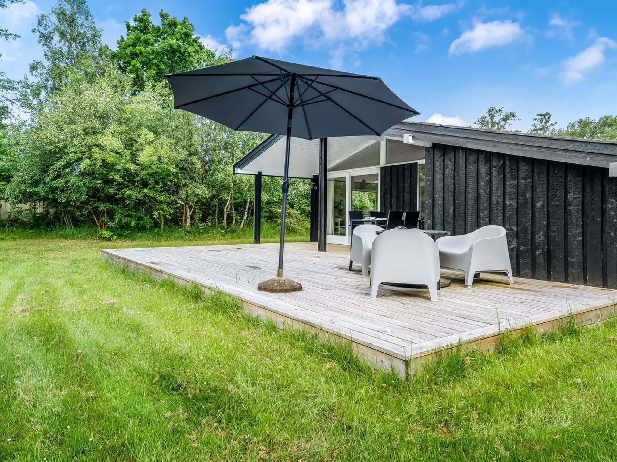Een modern terras buiten met een houten dek, een zwarte parasol en witte stoelen.