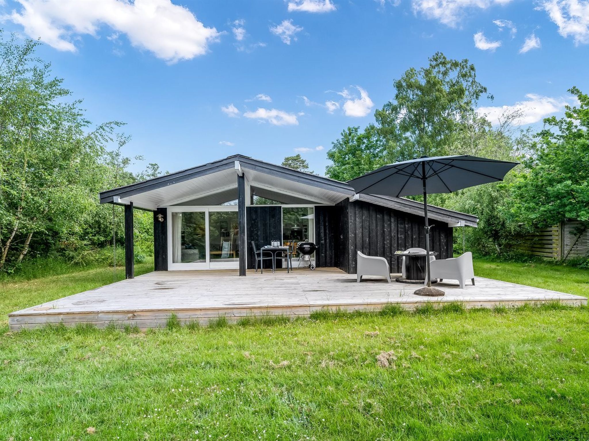 Une maison moderne dotée d’un patio couvert, d’un espace salon extérieur et d’un coin barbecue.