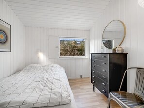 Cozy retreat with a single bed, white paneled walls, and a sloped ceiling, offering a view of the outdoors.