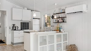 A modern kitchen with white cabinetry, a central island, pendant lights, and a built-in air conditioning unit.