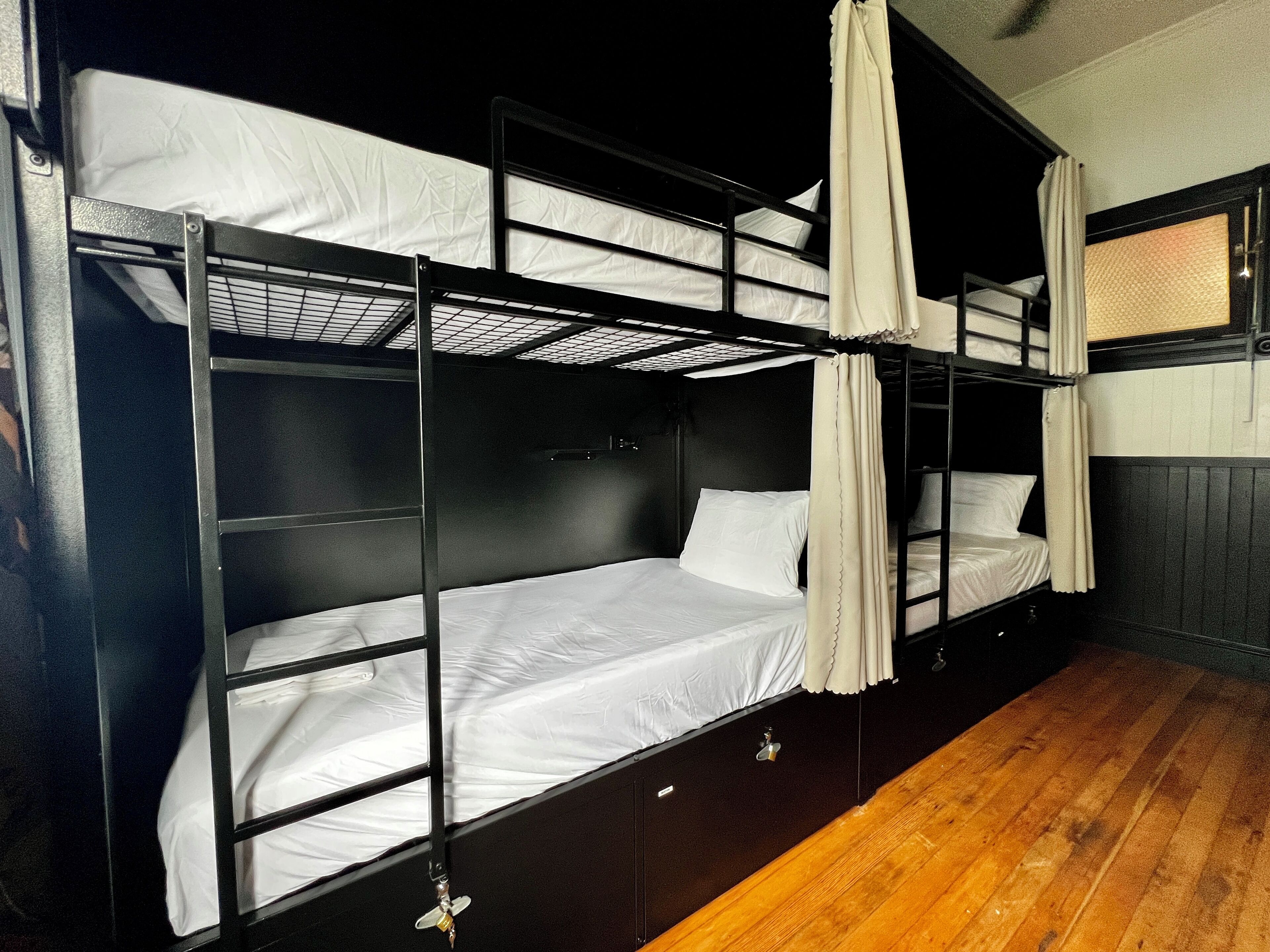 A bunk bed room with wooden flooring and a window with curtains.