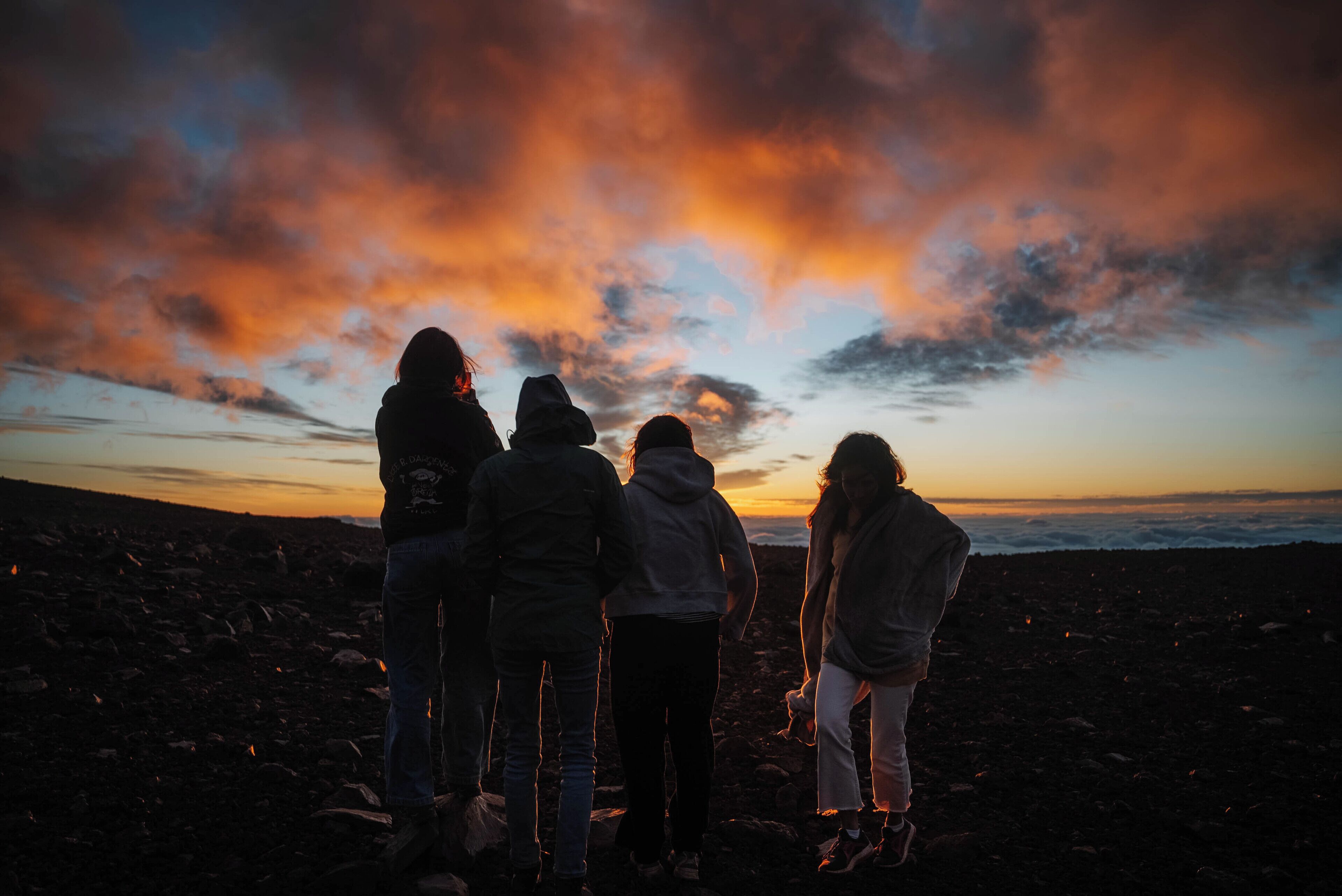 Four people standing on a rocky beach at sunset.