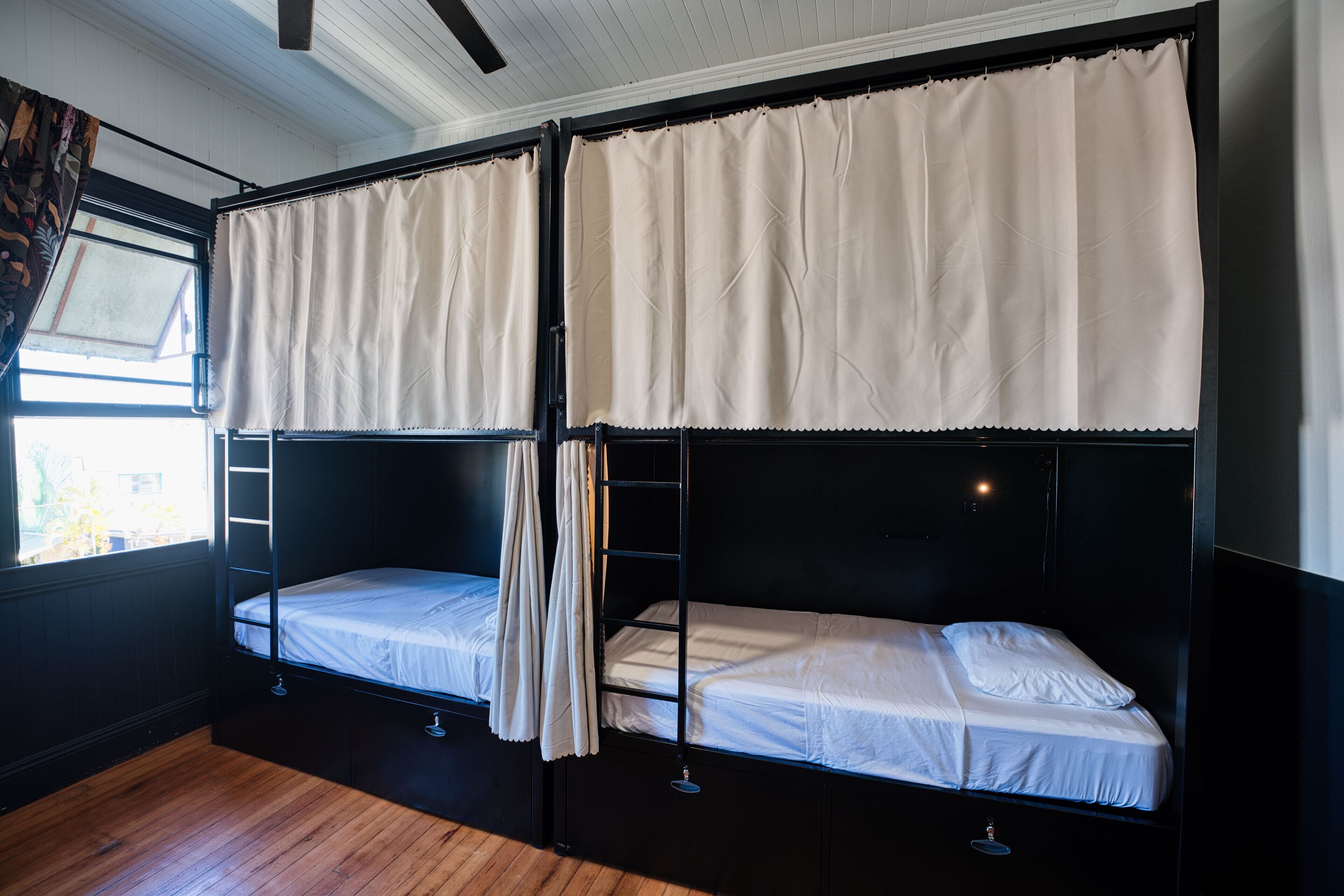 Une chambre avec deux lits superposés, un plancher en bois et une fenêtre avec des rideaux.