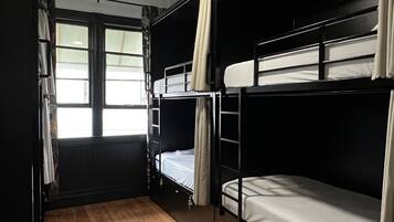 A bunk room with wooden flooring, a ceiling fan, and a window with curtains.