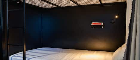 Un lit superposé avec un matelas et des oreillers, une lampe fixée au mur et une petite étagère avec un panneau.
