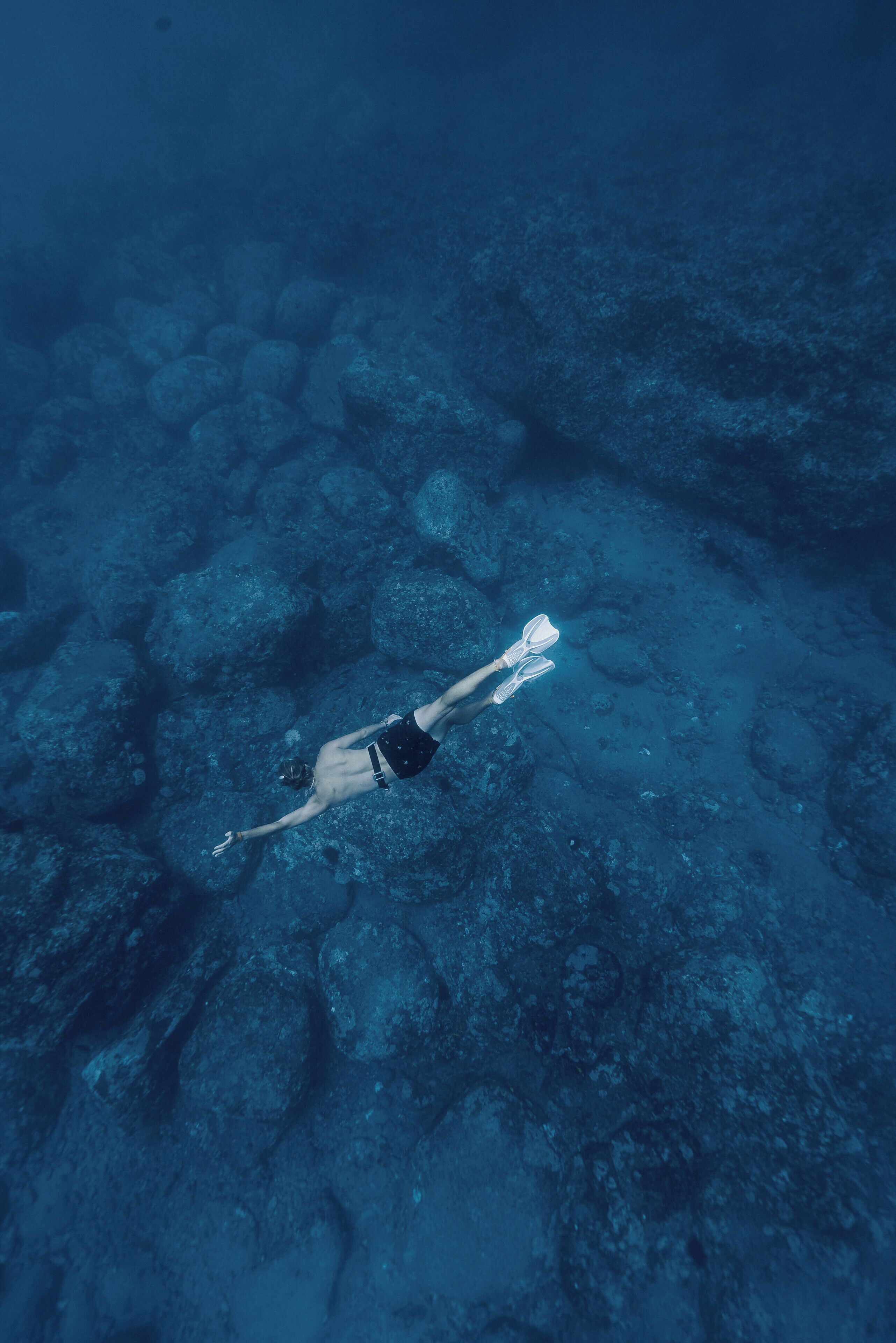 A person swimming underwater with rocks visible on the ocean floor.