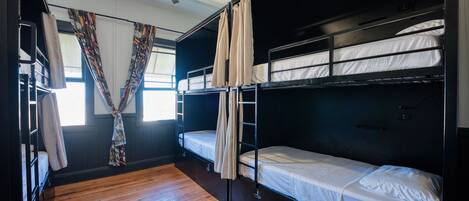 Un dormitorio con literas, suelo de madera, ventilador de techo y una ventana con cortinas.