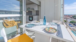 A balcony with a dining table set for two, a blue bottle, and a view of the city and sea. - Grand Bleu by Interhome (Le Barcarès)