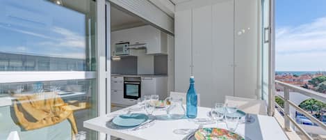 Ein Balkon mit Esstisch für zwei Personen, einer blauen Flasche und Blick auf Stadt und Meer.