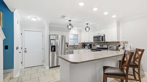 A modern kitchen with white cabinetry, a central island, stainless steel appliances, and a blue accent wall. - 135 Grande Island Blvd  - Dog Friendly (Panama City Beach)
