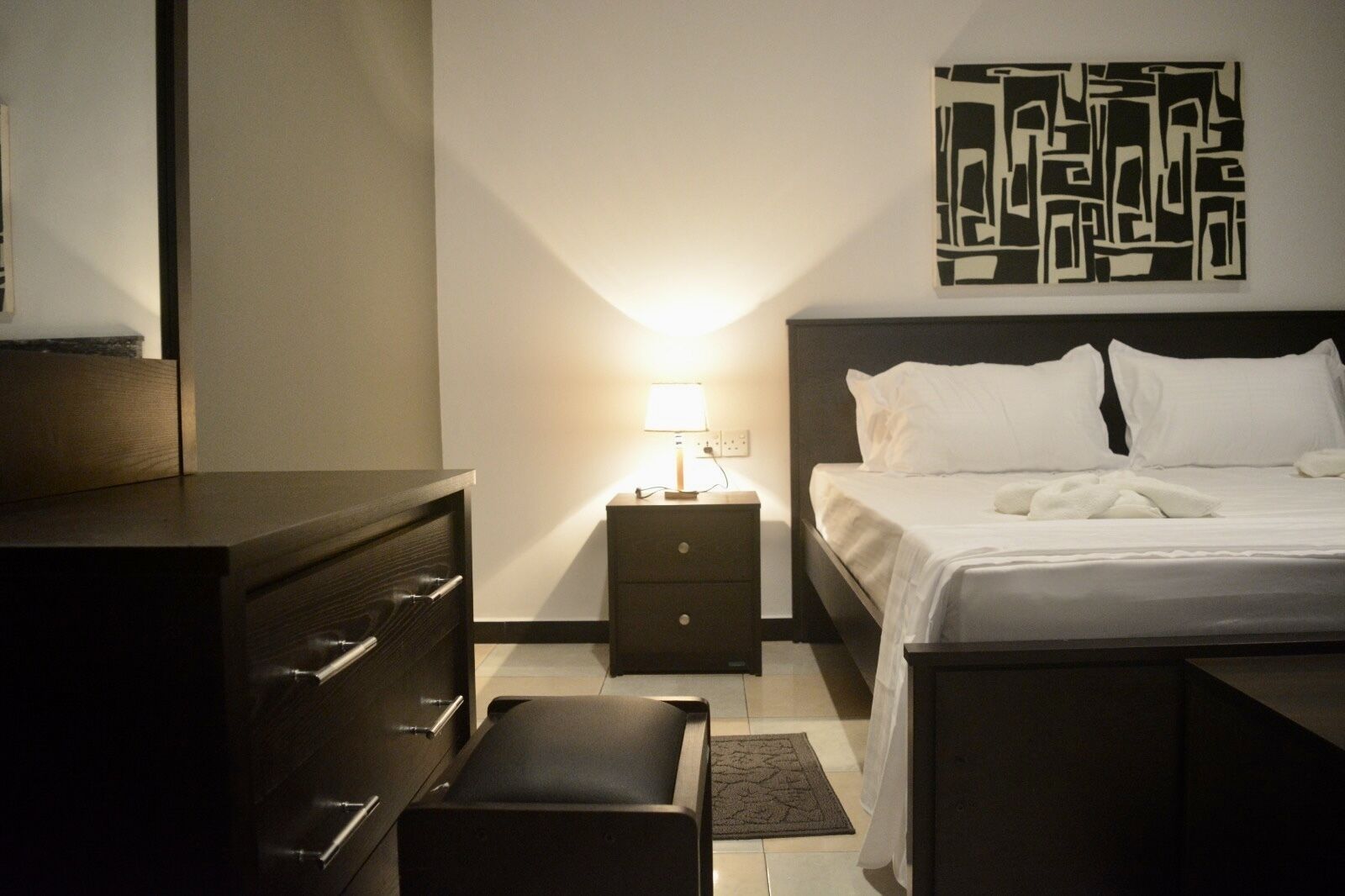 Une chambre d’hôtel comprenant un lit, une table de chevet avec une lampe, une commode et une œuvre d’art murale.