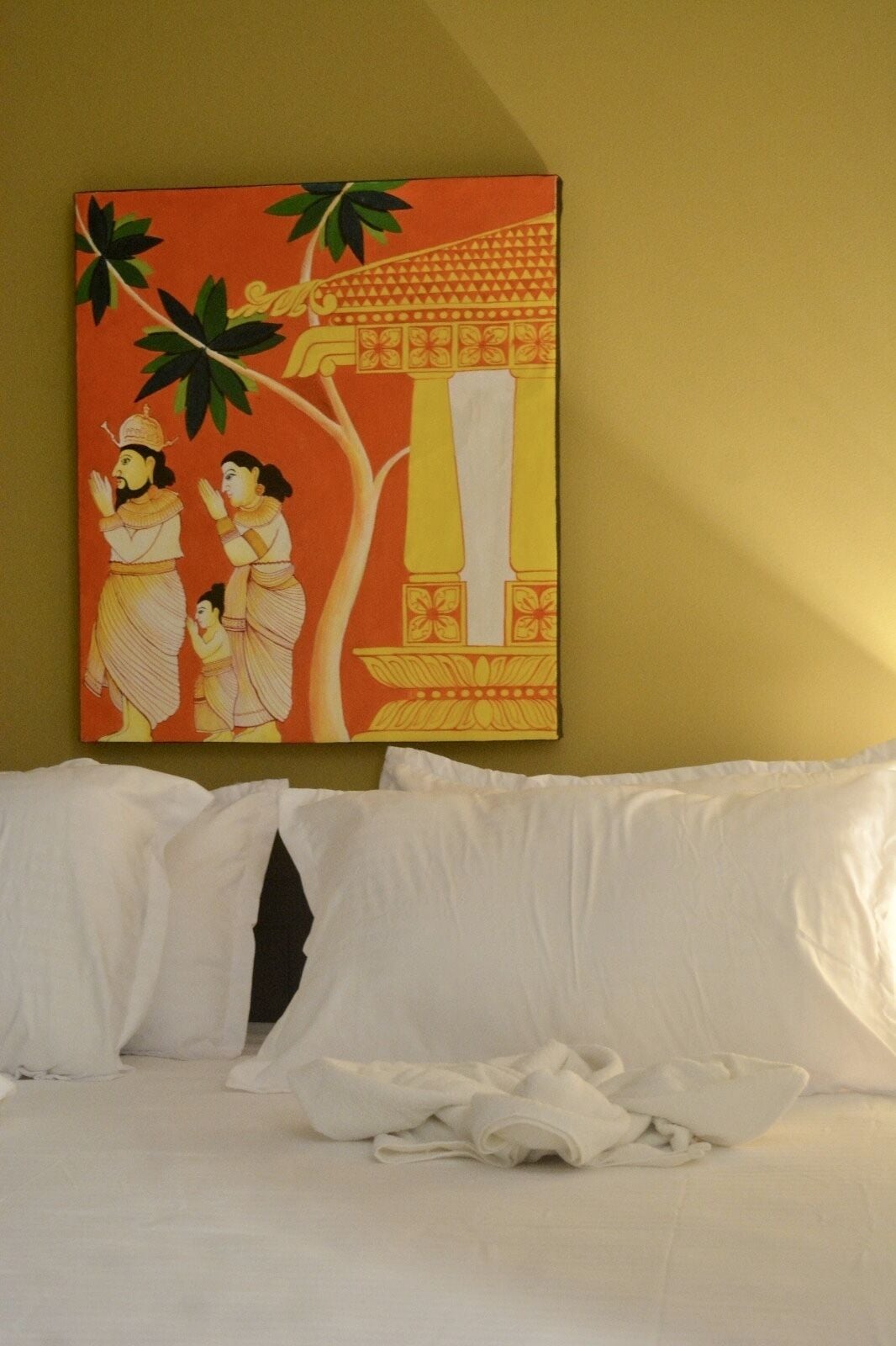 Habitación de hotel con cama, almohadas blancas y un cuadro en la pared que representa una escena tradicional.